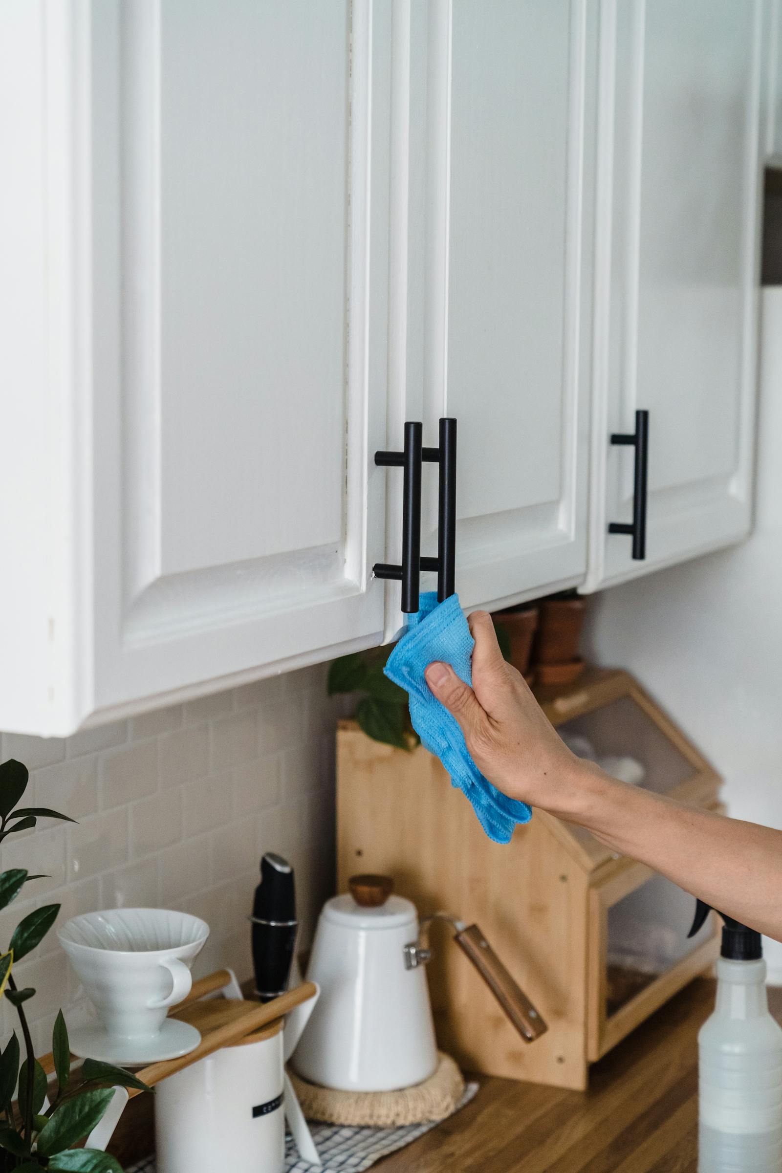 A person wiping kitchen cabinet handles in a clean modern kitchen, representing easy-maintenance design.